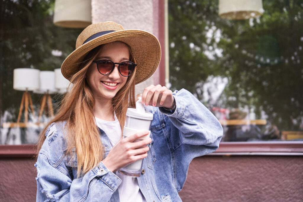 Pretty girl with eco coffee cup. Drinking beverage outdoors.