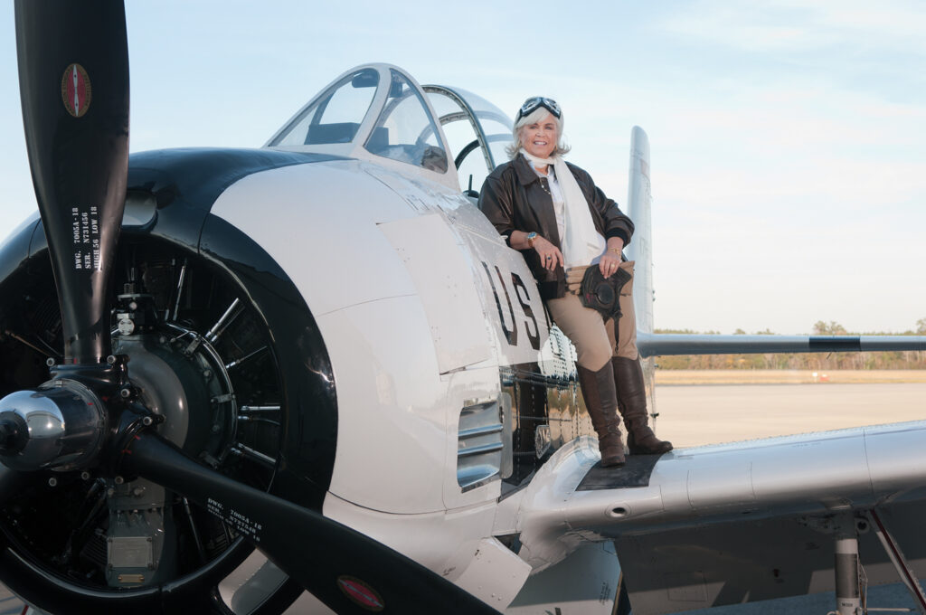 Pat Bradford on location with Bill Cherry’s 1953 North American Aviation T-28, on the ramp at Air Wilmington in 2016. The T-28 is a radial-engine trainer aircraft that was used by the U.S. Air Force and Navy. Pat’s hair by Frank Potter, Bangz Hair Salon, Wilmington. WBM File Photo
