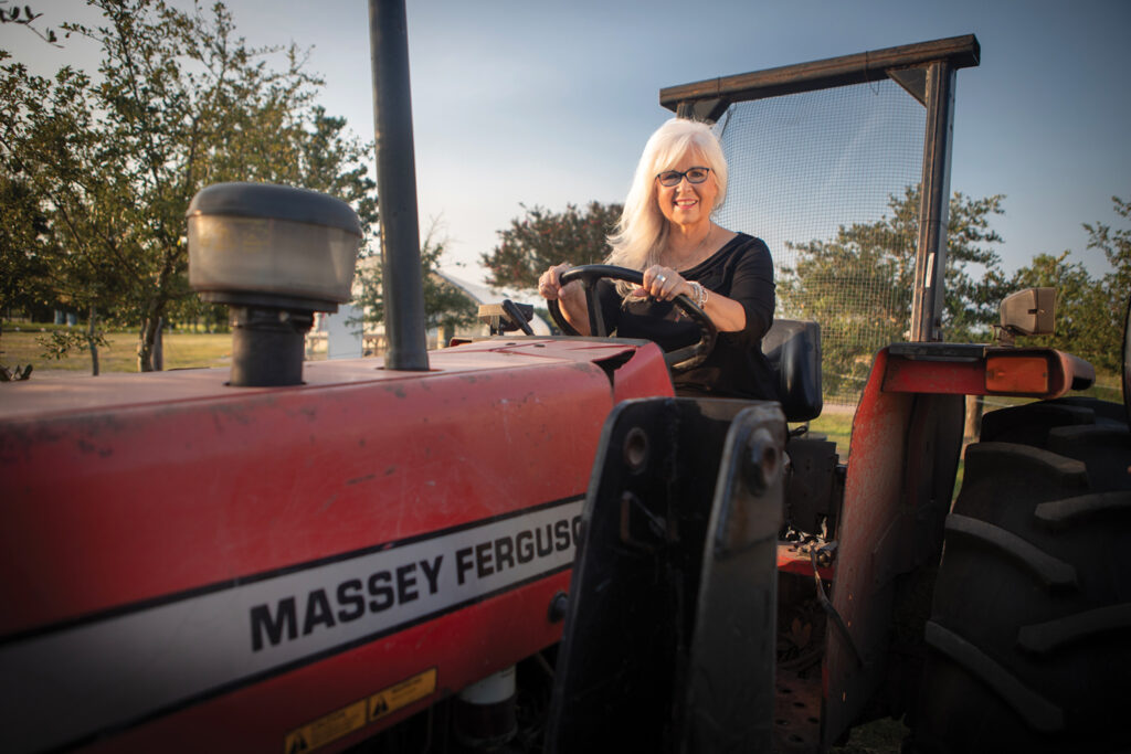 Pat Bradford at Penderlea Farms in August 2023 on a Massey Ferguson 383 utility tractor, one of the farm’s selection of tractors. A little-known bit of trivia about Bradford is her affection for tractors. Pat Bradford’s hair by Frank Potter, hair styled by Victoria Paz, makeup by Ken Grimsley, Bangz Hair Salon. Steve McMillan