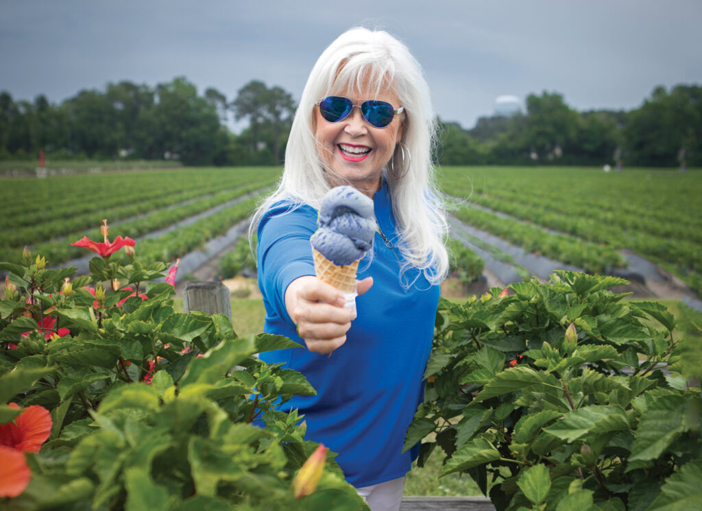 Pat Bradford enjoys a long-standing start of the summer ritual at Lewis Farms on Gordon Road. Seen here in front of the u-pick strawberry and blueberry fields with a Lewis Farms homemade triple blueberry ice cream cone. Pat Bradford’s hair by Frank Potter, hair styled by Victoria Paz, and makeup by Ken Grimsley, all with Bangz Hair Salon. Steve McMillan